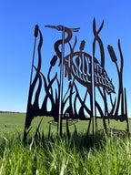 Black metal yard sculpture of a heron among reeds, displayed outdoors in a grassy field under a clear blue sky.