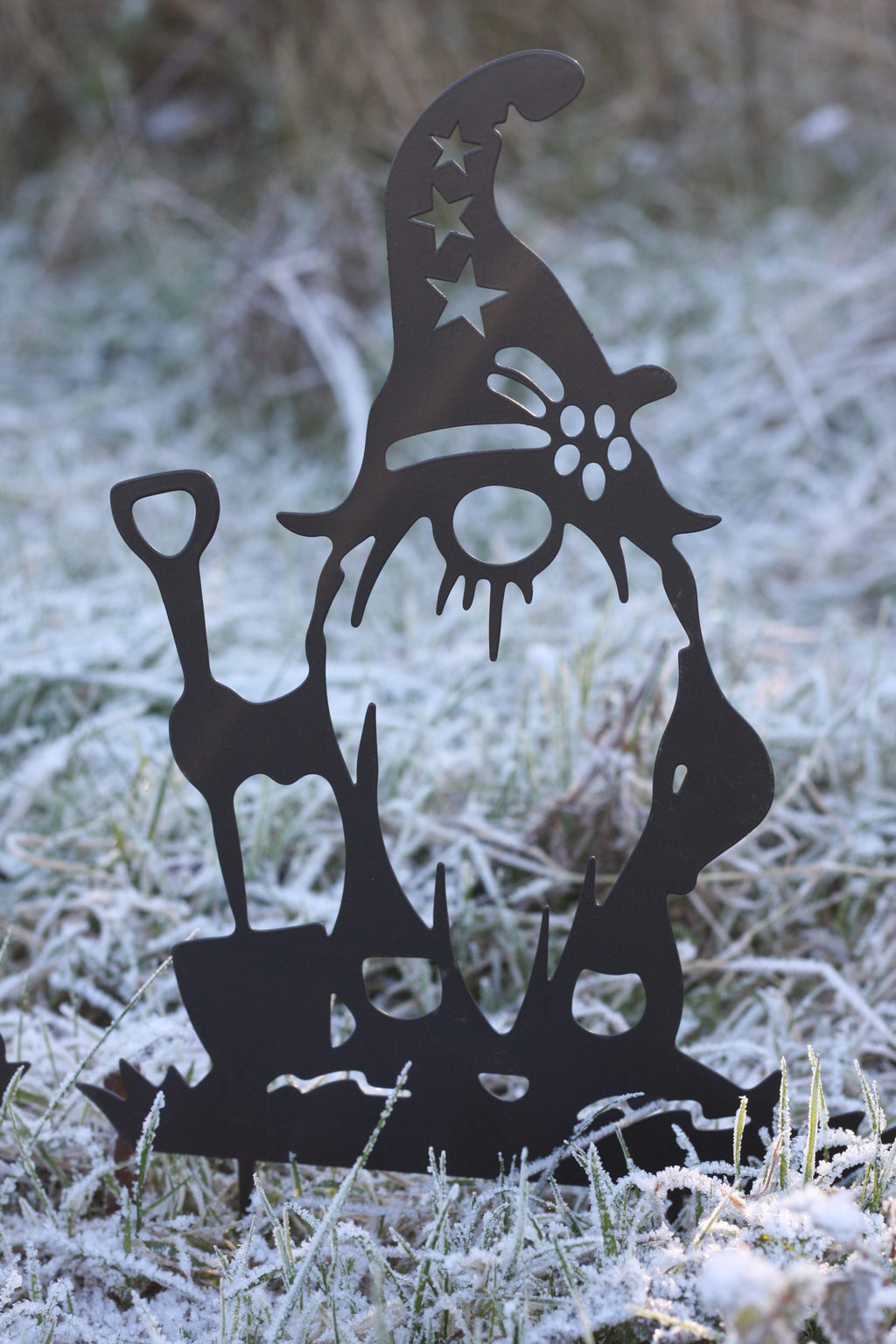 A black metal garden gnome silhouette decoration standing in frosty grass outdoors.