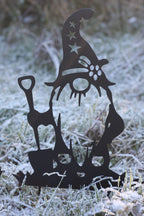 A black metal garden gnome silhouette decoration standing in frosty grass outdoors.