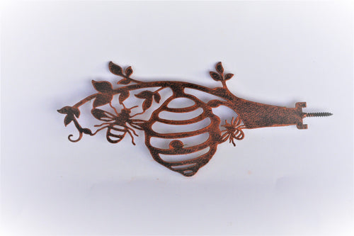 A rusted metal wall hook shaped like a beehive with bees and leaves, shown against a plain white background.