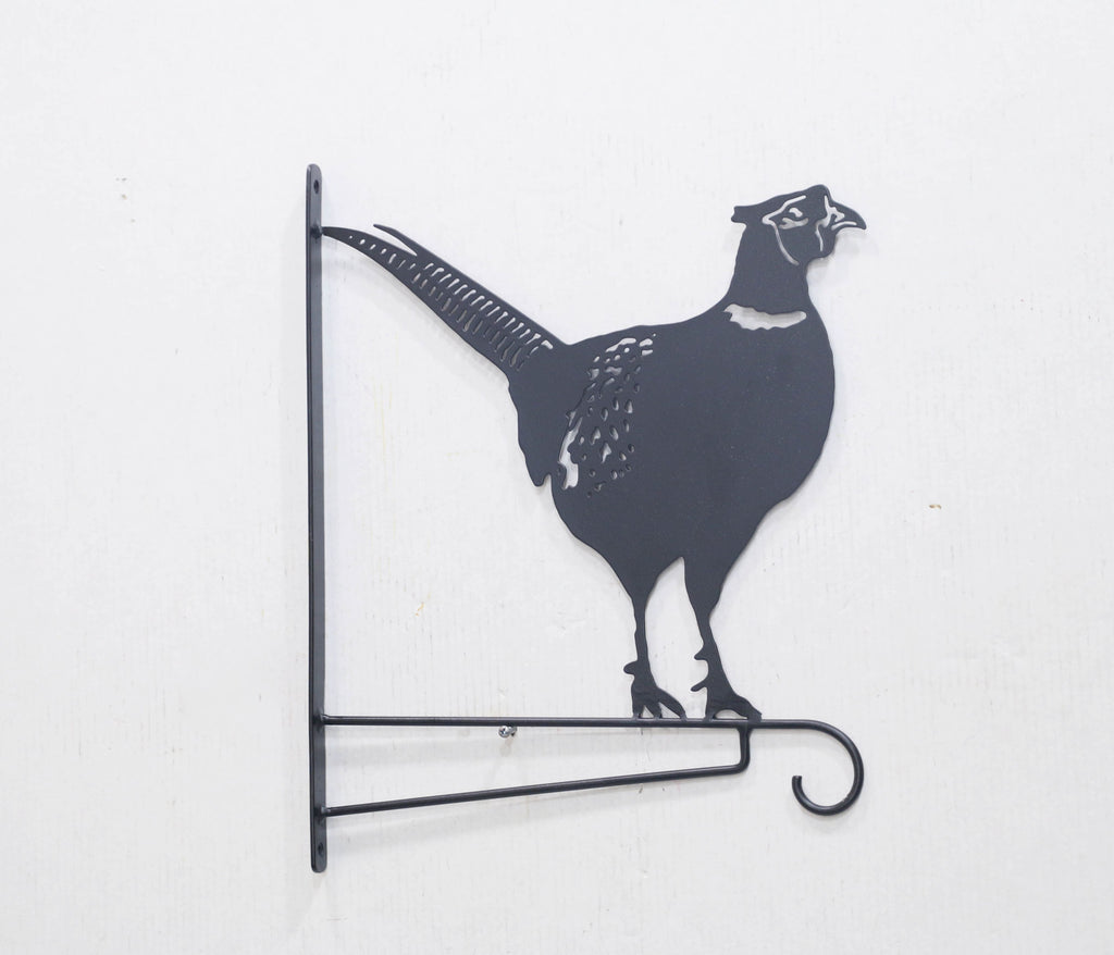 Black metal wall decor shaped like a pheasant bird, mounted on a white wall with a horizontal hook at the bottom.