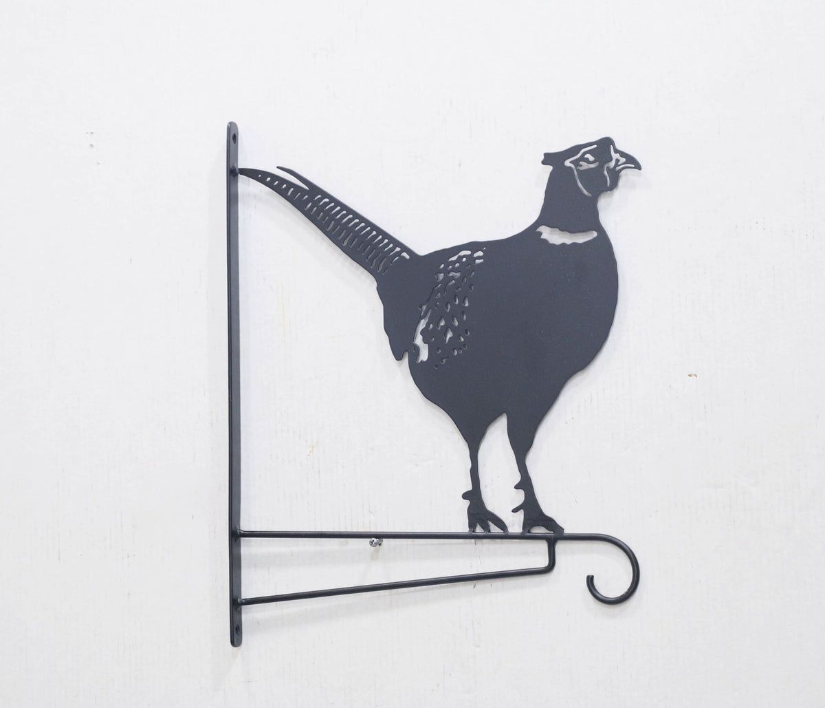 Black metal wall decor shaped like a pheasant bird, mounted on a white wall with a horizontal hook at the bottom.