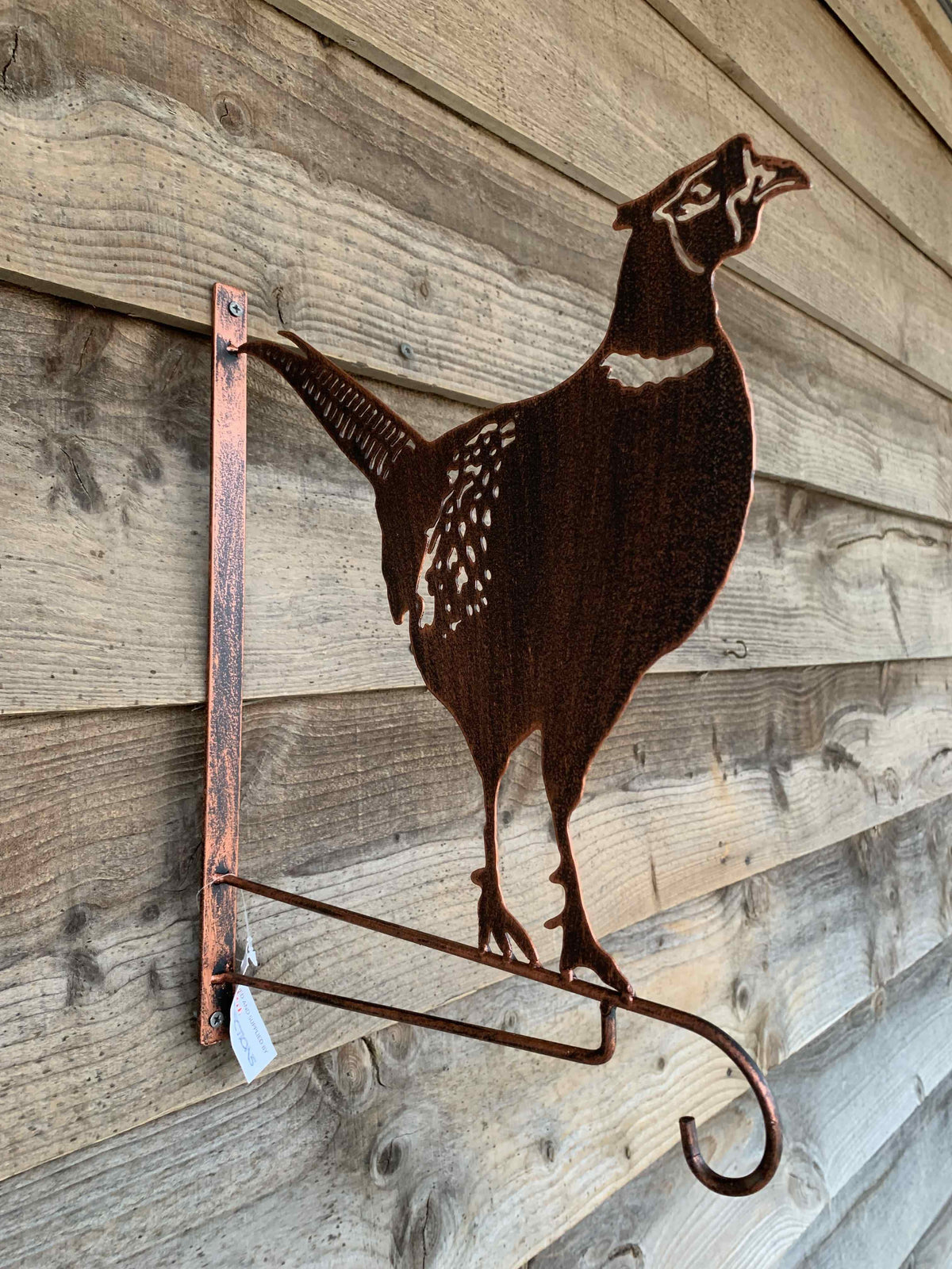 A rustic metal wall sculpture of a walking cat made from coppery-brown steel, displayed on a weathered wooden plank surface.