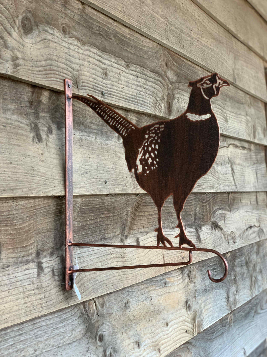 A rustic metal wall hook shaped like a pheasant bird, mounted on a weathered wood plank wall.