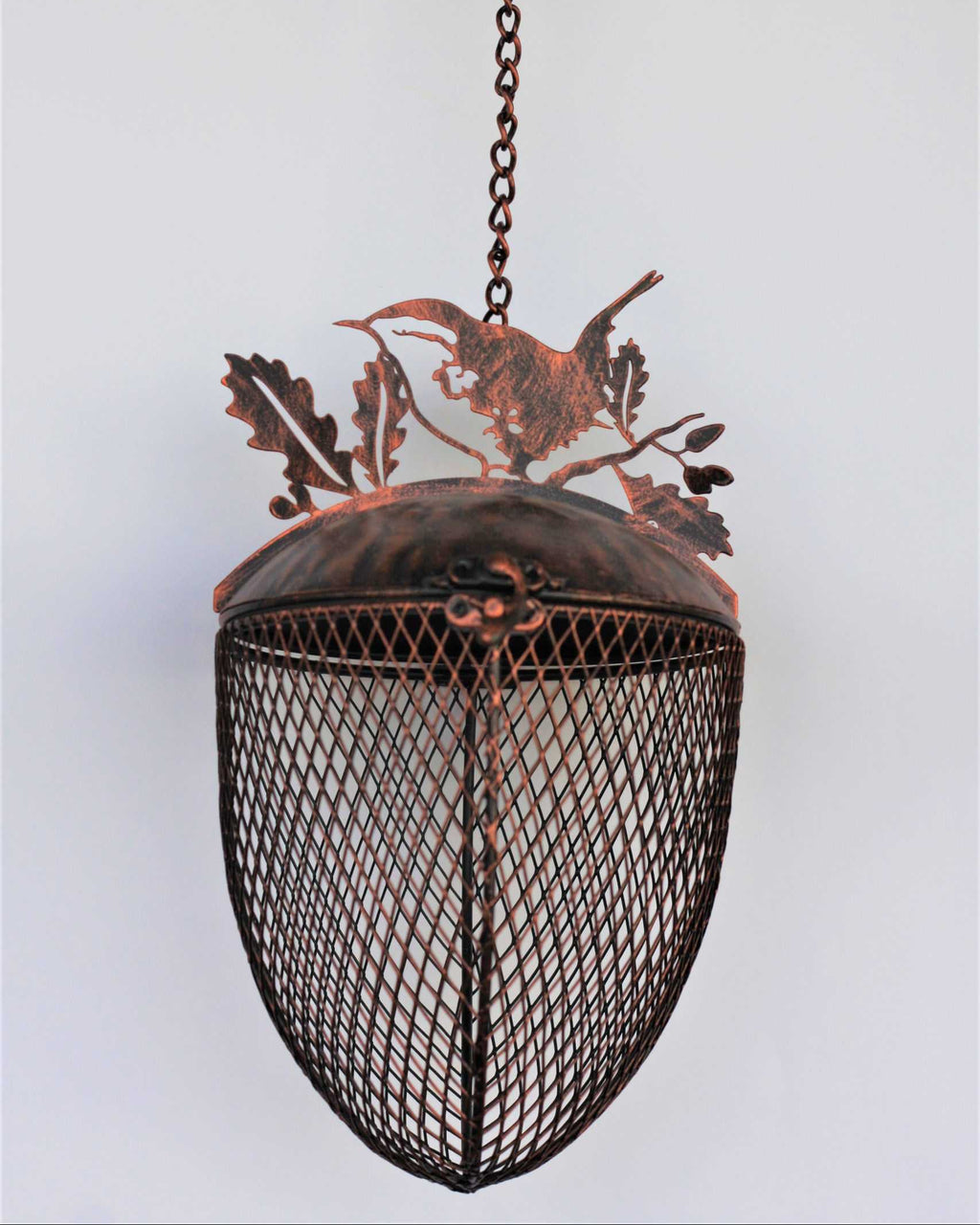 A rustic metal hanging bird feeder with a copper-toned top and a dark mesh-covered shade, suspended by a chain from a hook against a plain light background.