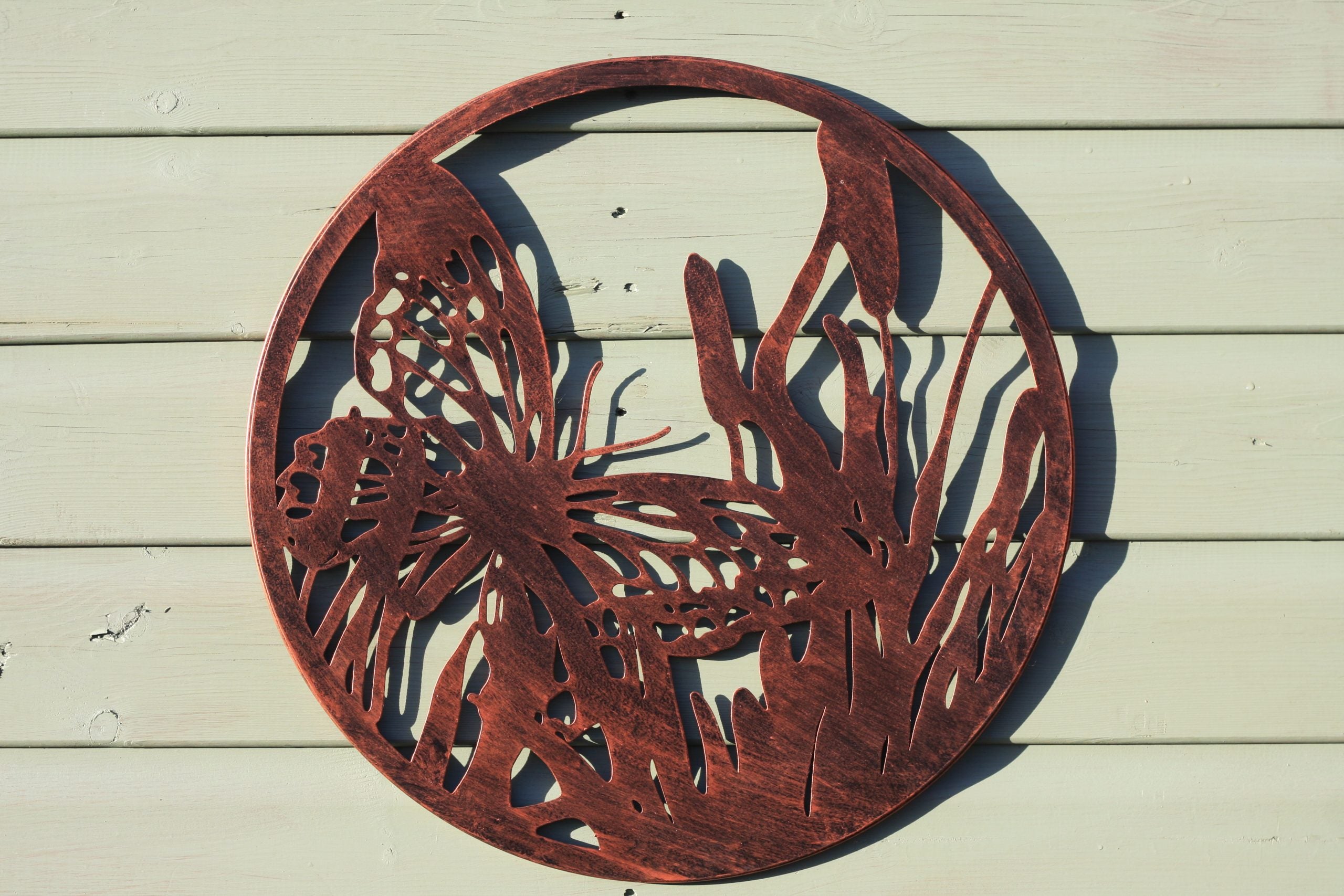Decorative metal wall art with butterfly design on a wooden surface