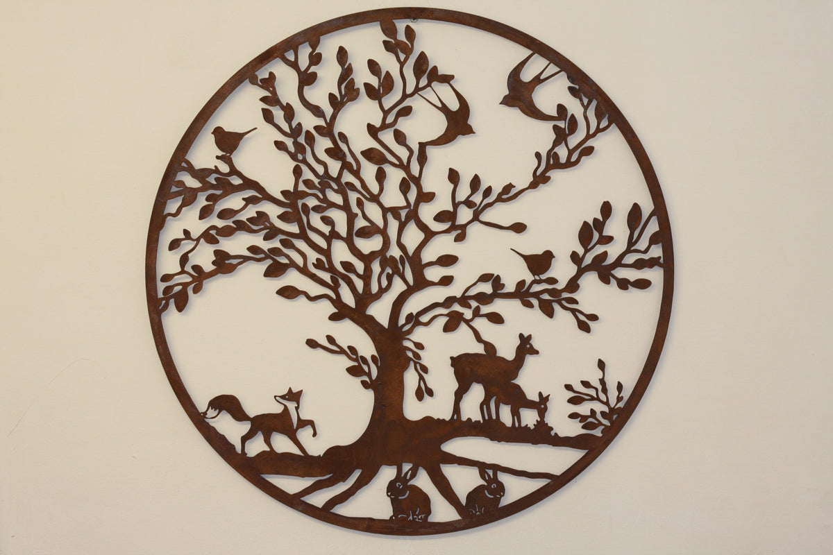 Round laser-cut metal wall art featuring a tree with birds, deer, and rabbits, shown against a plain off-white wall.