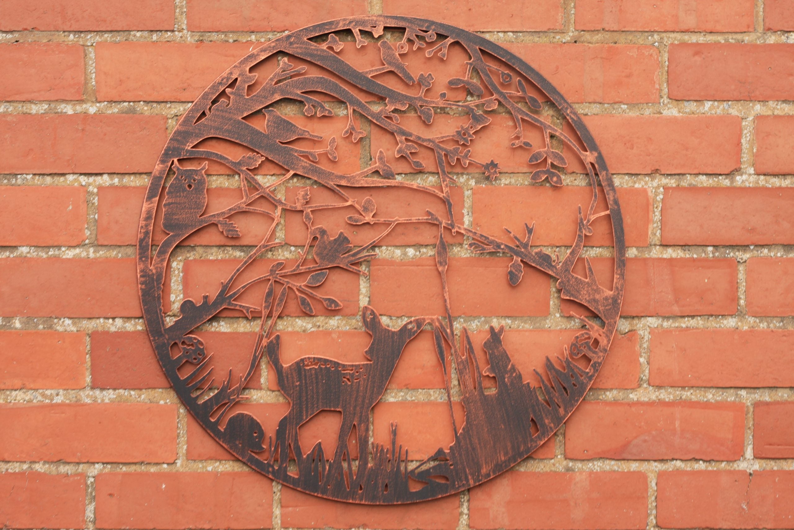 Decorative metal wall art with deer and nature elements on a brick wall