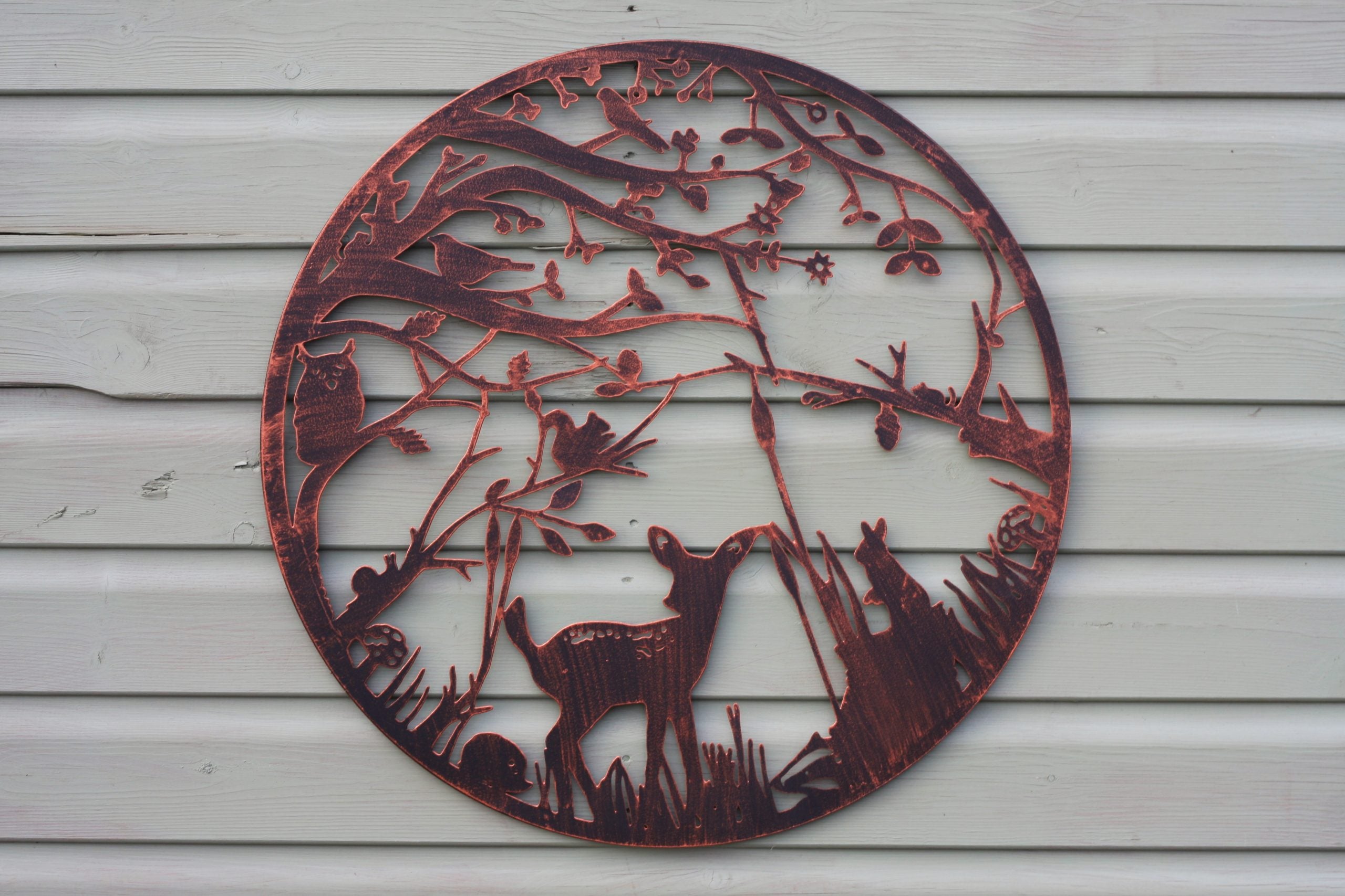Round metal wall art with deer design on a wooden surface