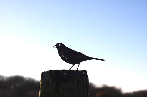 A black metal bird silhouette sculpture perched on a wooden post against a clear blue sky.