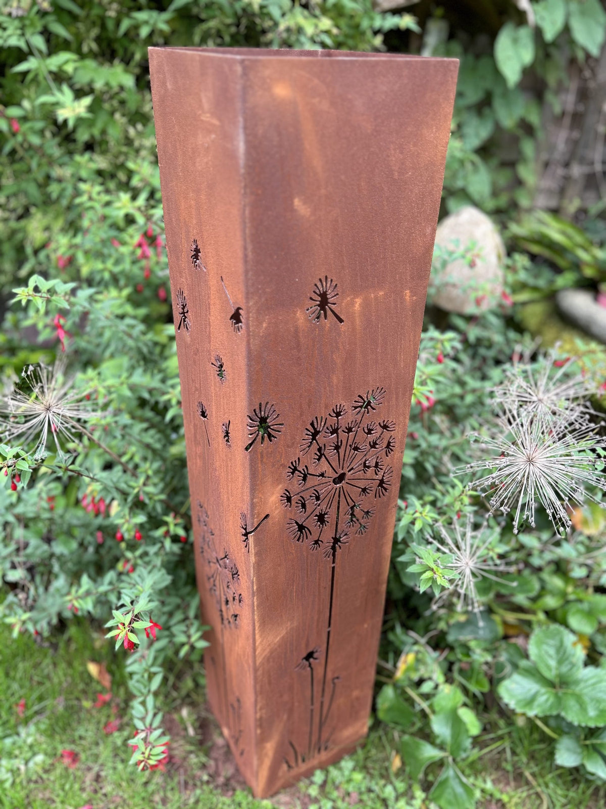 Corten steel planter with dandelion design in a garden setting