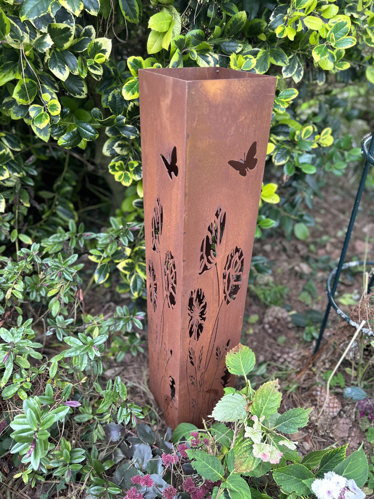 Copper-colored garden lantern with butterfly designs on a green leafy background