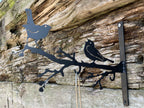 Black metal wall decor featuring two birds perched on a branch, mounted on a rustic weathered wood wall.