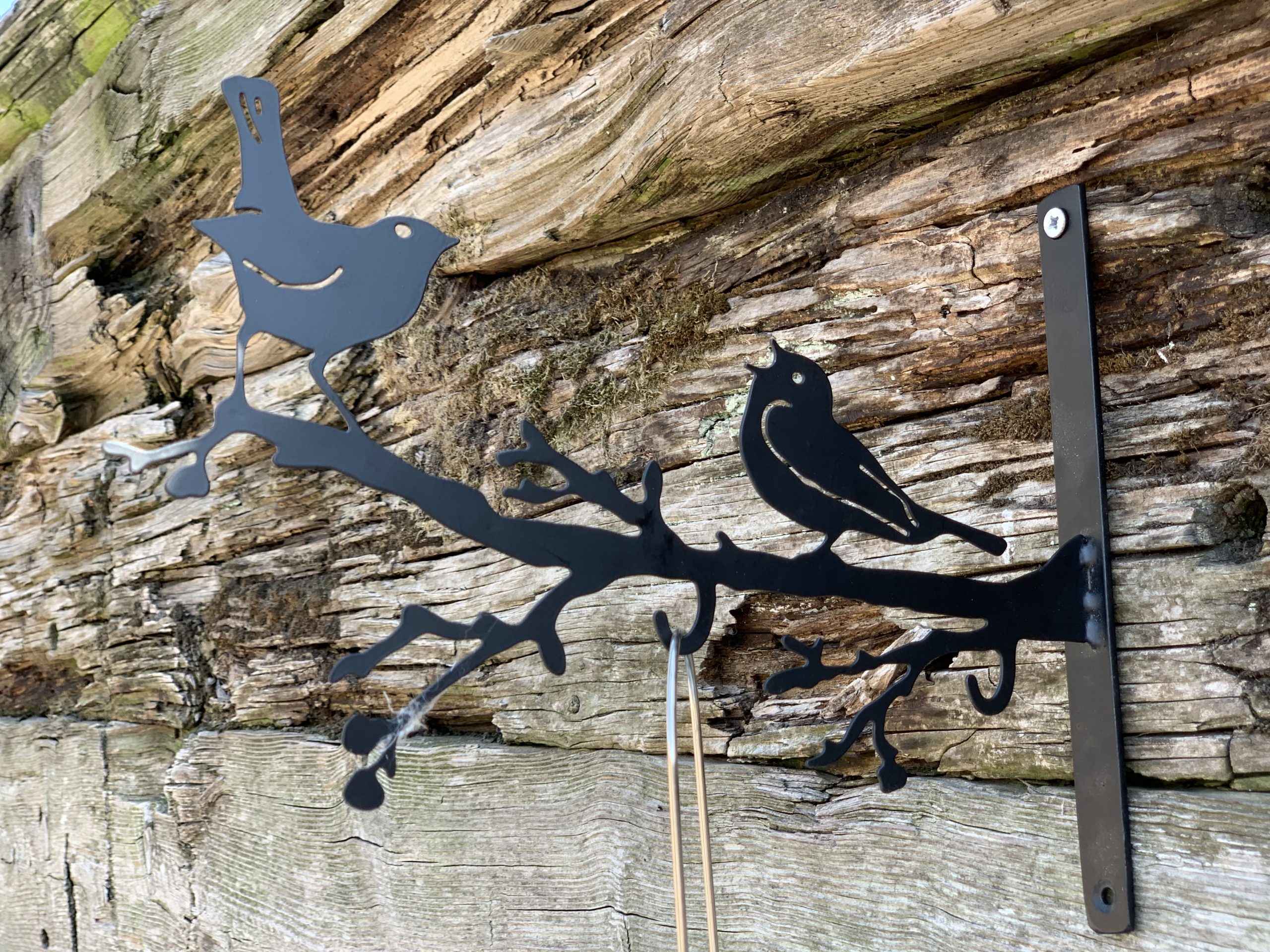 Black metal wall decor featuring two birds perched on a branch, mounted on a rustic weathered wood wall.