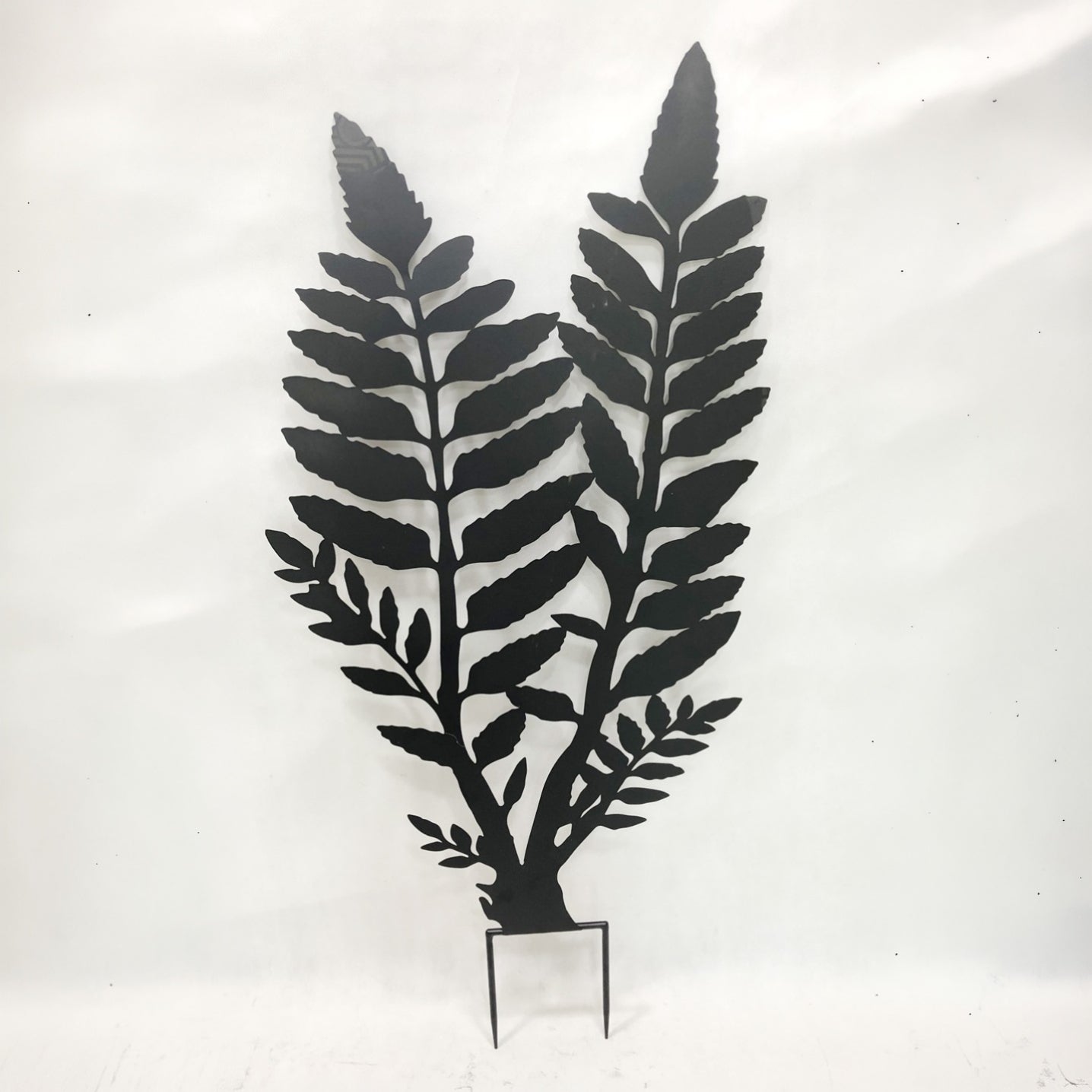Black metal fern wall decor with a small metal stand, shown against a plain white background.