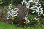 A dark brown metal garden stake shaped like a rabbit with decorative cutout details, placed in a grassy garden bed surrounded by white daisies.