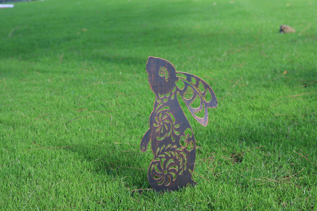 A decorative metal garden stake shaped like a rabbit with wings, standing upright in a green grass lawn.