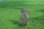 A decorative metal garden stake shaped like a rabbit with wings, standing upright in a green grass lawn.