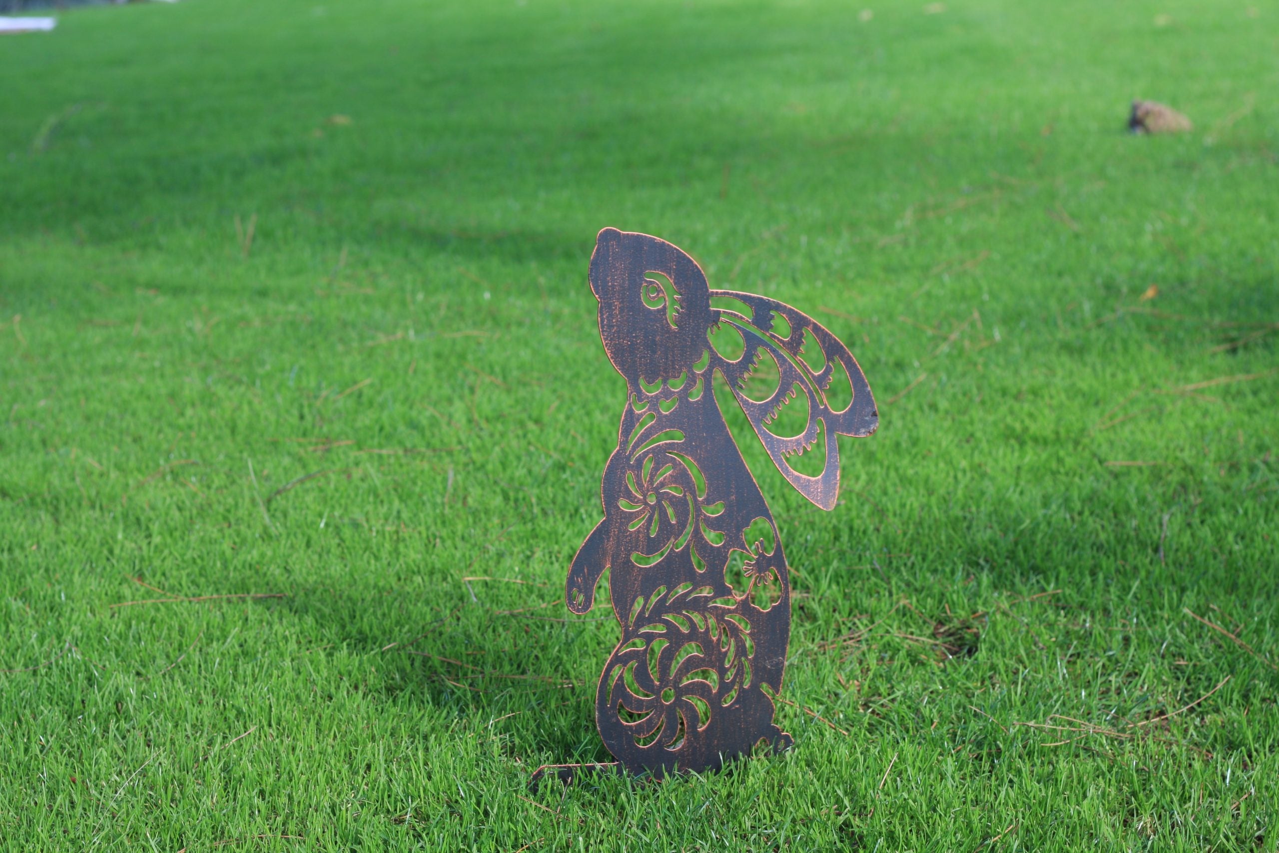 A decorative metal garden stake shaped like a rabbit with wings, standing upright in a green grass lawn.