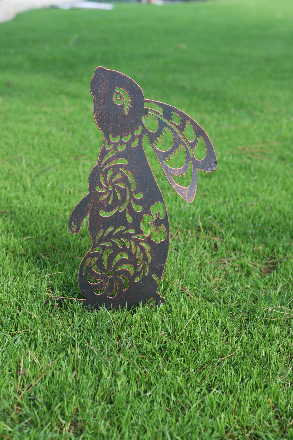 A decorative metal garden stake shaped like a rabbit with cutout floral patterns, standing upright in a green grass lawn.