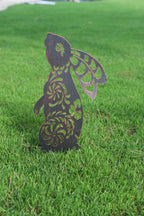 A decorative metal garden stake shaped like a rabbit with cutout floral patterns, standing upright in a green grass lawn.