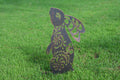 A decorative metal garden stake shaped like a rabbit with intricate cutout patterns, standing upright on a green grass lawn.