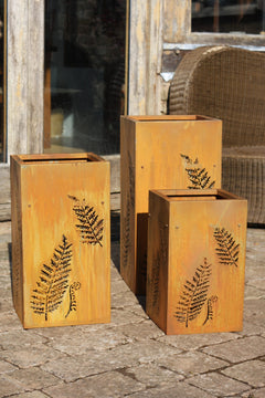 Three rust-colored planters with fern designs on a stone patio.