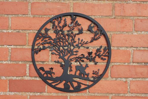 A circular black metal wall art piece featuring a tree with animals and birds, mounted on a red brick wall.