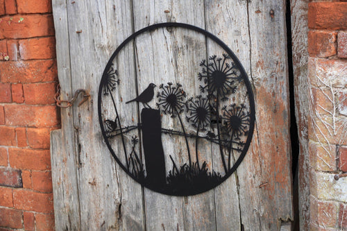 Decorative metal wall art of a bird and dandelions on a wooden panel with a brick background.
