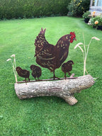 A metal garden sculpture of a mother hen and three chicks standing on a log, placed on a green lawn.