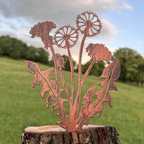 Copper metal dandelion garden stake mounted on a rustic tree stump, photographed outdoors against a blurred green lawn and blue sky.