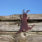 A rusted metal cutout of a jumping rabbit mounted on a weathered wooden surface under a clear blue sky.