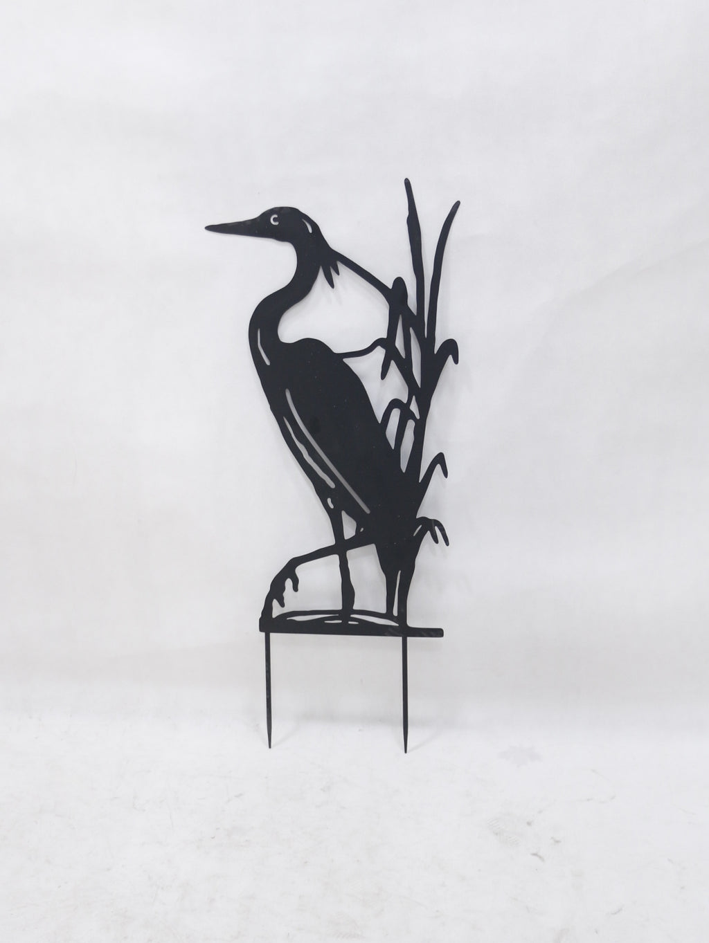 Black metal garden stake featuring a heron standing among reeds, mounted on two thin stakes against a plain white background.